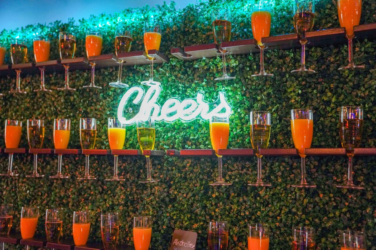 Sektempfang vor grüner Wand mit Cheers-Leuchtschrift