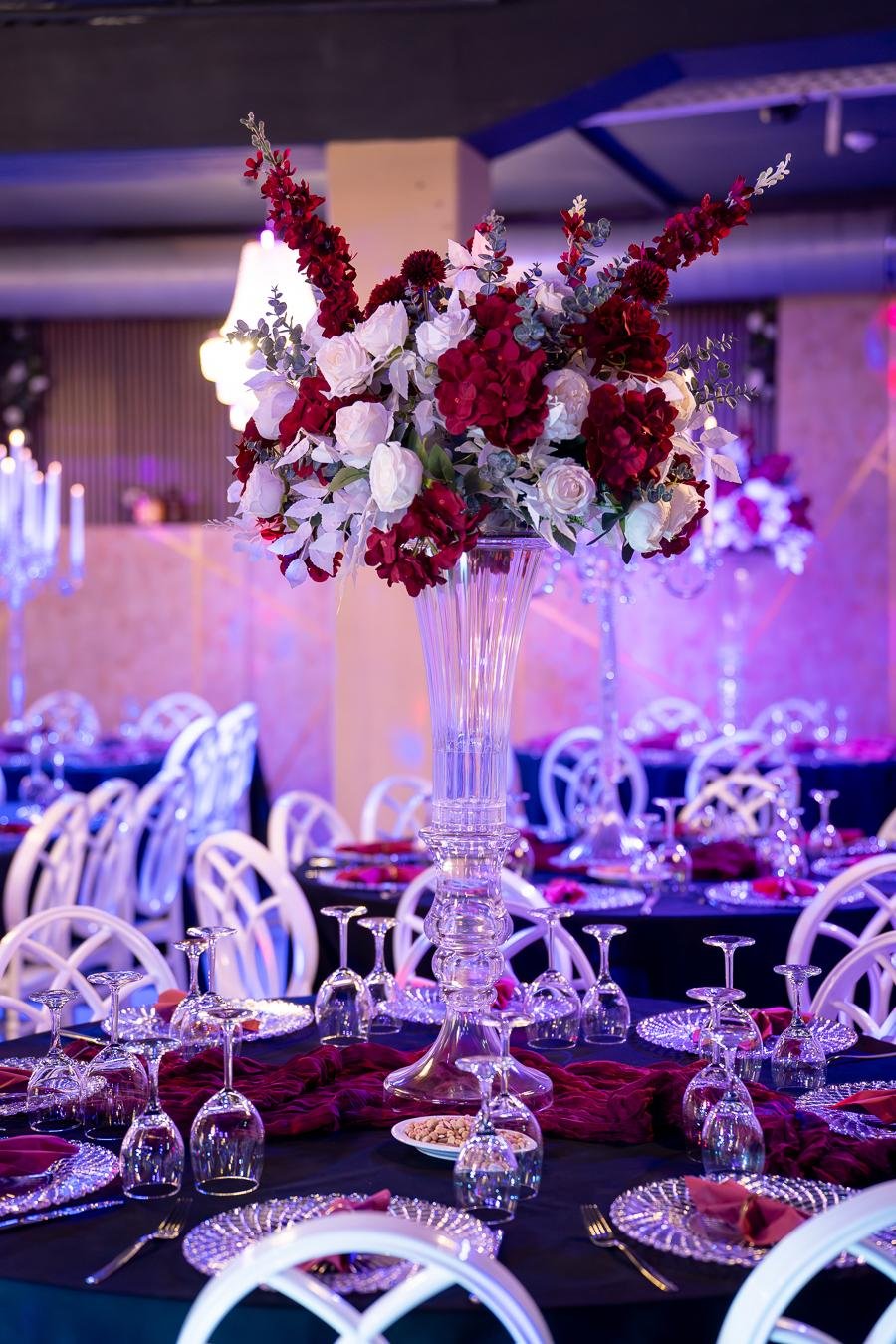 Tischdekoration mit roten und weißen Rosen in hoher Kristallvase auf einer Hochzeitstafel
